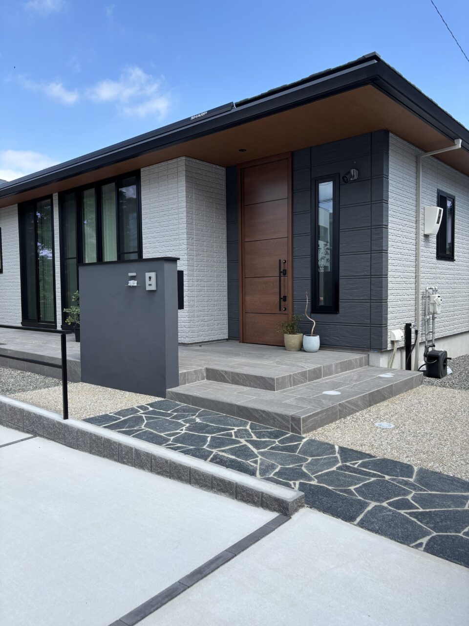 福岡市中央区の新築外構アプローチ写真。東洋工業「オークルストーン パールブラック」を乱形で施工し、平屋住宅の直線的な外観にやわらかさと動きを添えたデザイン。段差を抑えた安心の動線設計。｜ウェルミカ