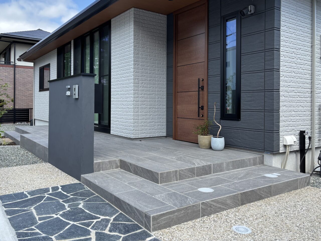 福岡市中央区の新築外構。玄関ポーチとお庭のタイルデッキを一体化し、回遊できる動線を実現。平屋住宅の外観に合わせたグレー調タイルが上質で調和のとれたデザイン。｜ウェルミカ