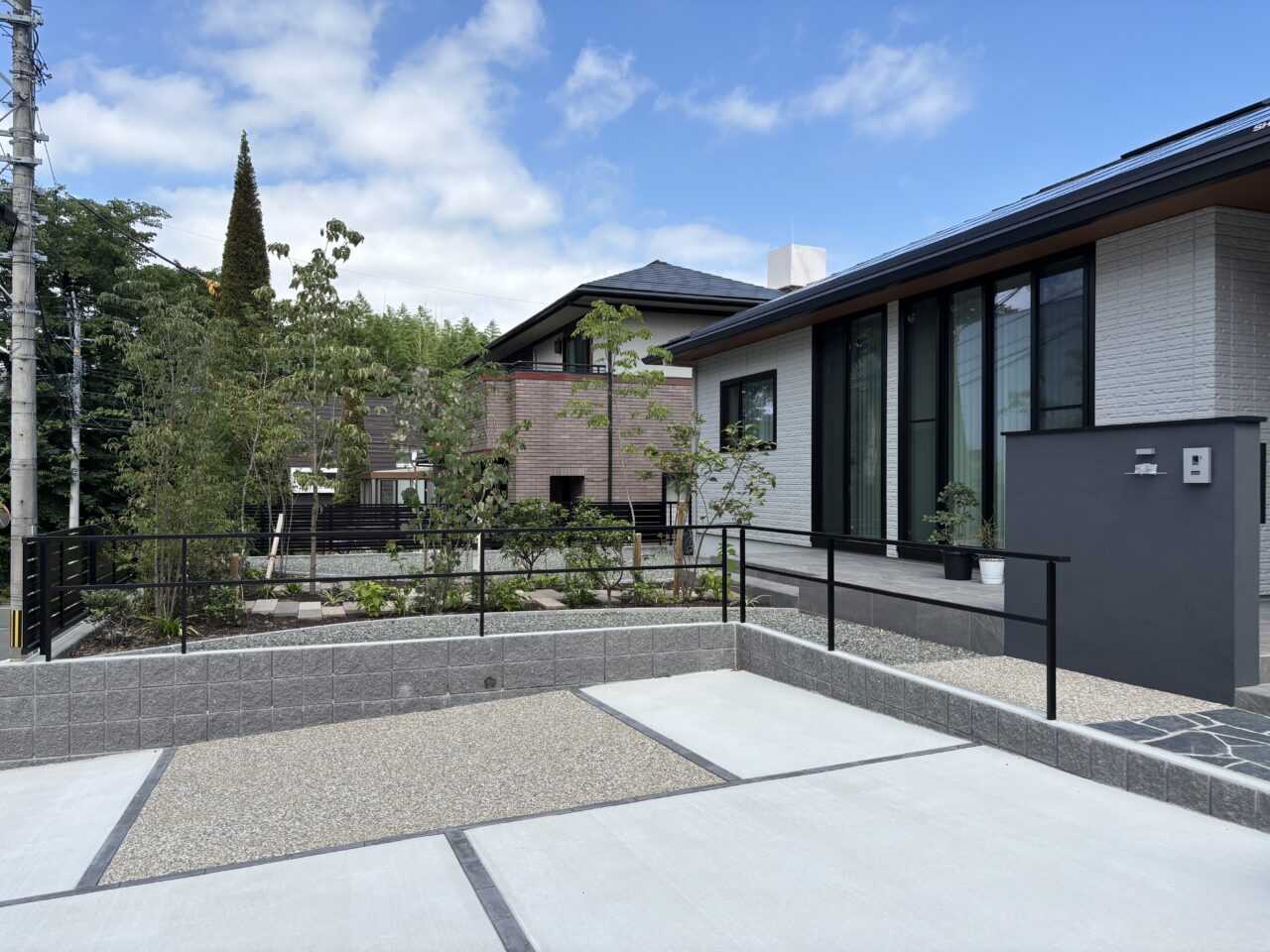 福岡市中央区の新築外構。駐車スペース・門柱・植栽・タイルデッキが調和した全景。平屋住宅に寄り添うナチュラルモダンなデザインが上質な印象を与える。｜ウェルミカ