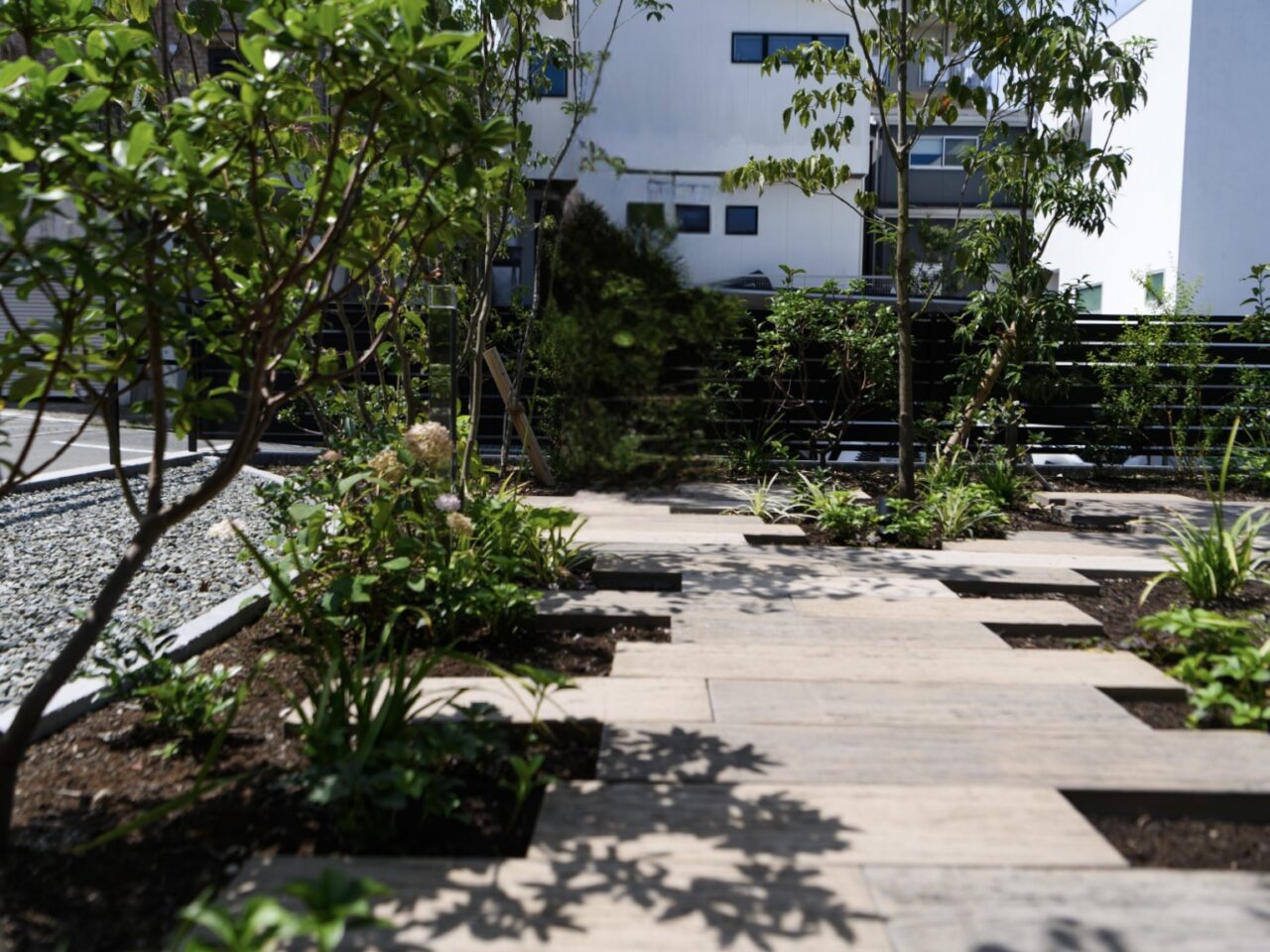 福岡市中央区の新築外構。東洋工業「レイルスリーパー ペイブライト」で仕上げた木目調の枕木アプローチと、四季を彩る植栽がやさしい印象を与えるお庭。｜ウェルミカ