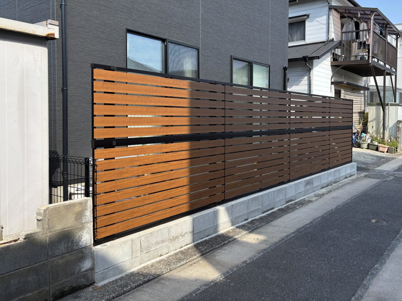 福岡市東区で施工したYKKルシアスフェンスYS2H型（キャラメルチーク×カームブラック）。道路側から見た目隠しフェンスの全体外観｜ウェルミカ