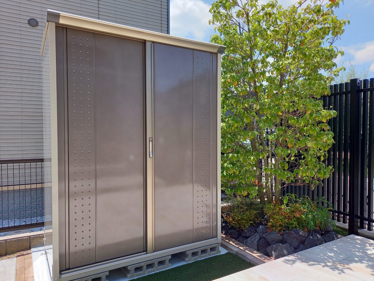 福岡県北九州市小倉南区の外構リフォームで設置したタクボ物置「グランプレステージ」。シンプルでモダンなデザインが庭全体と調和し、収納力と美観を両立しています。