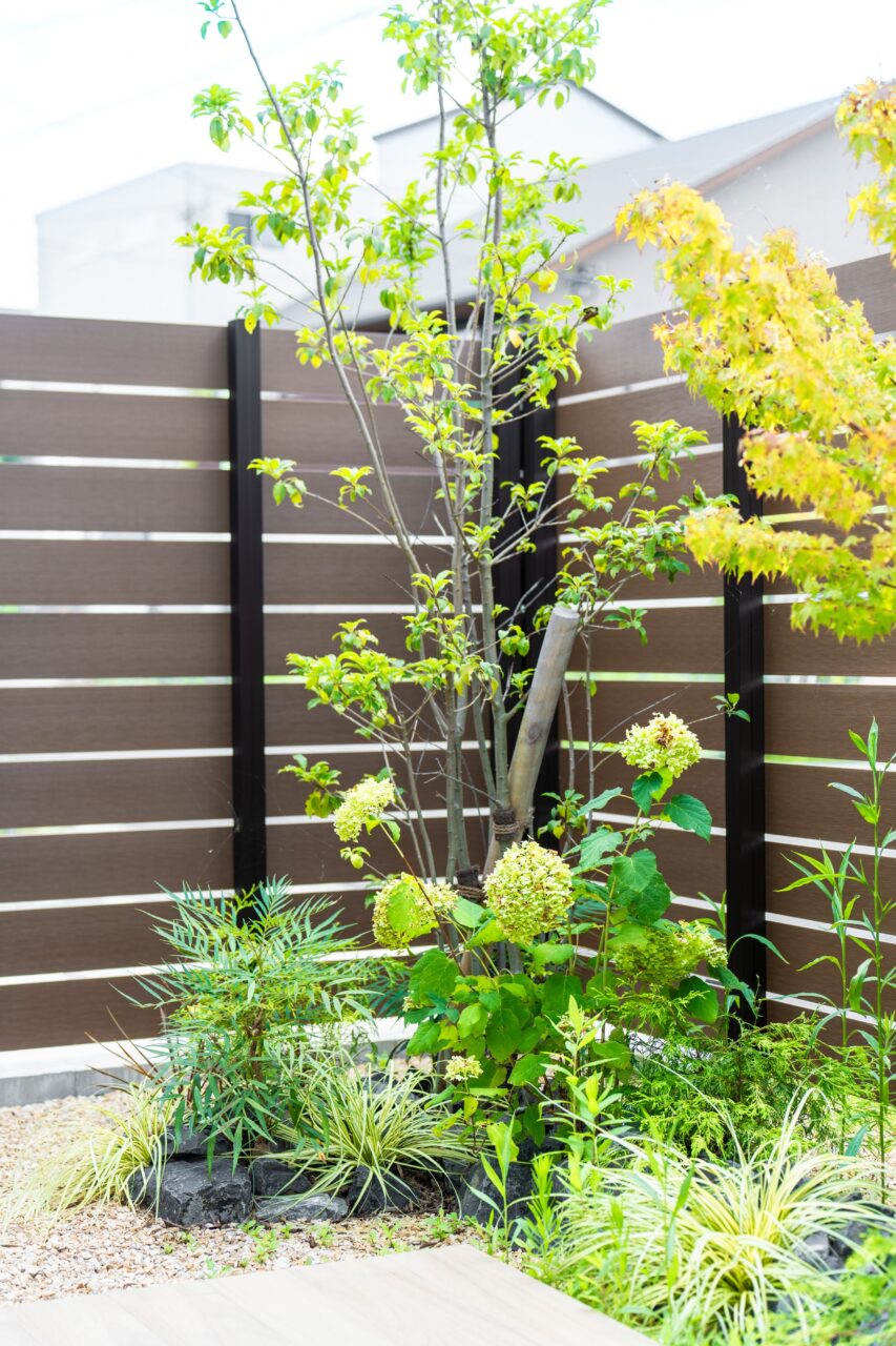 岡垣町で施工した外構リフォームの植栽写真｜東洋工業『和石・揖斐』の花壇にモミジとソヨゴを配し、ブラウン系フェンスやタイルと調和したナチュラルモダンの庭｜ウェルミカ