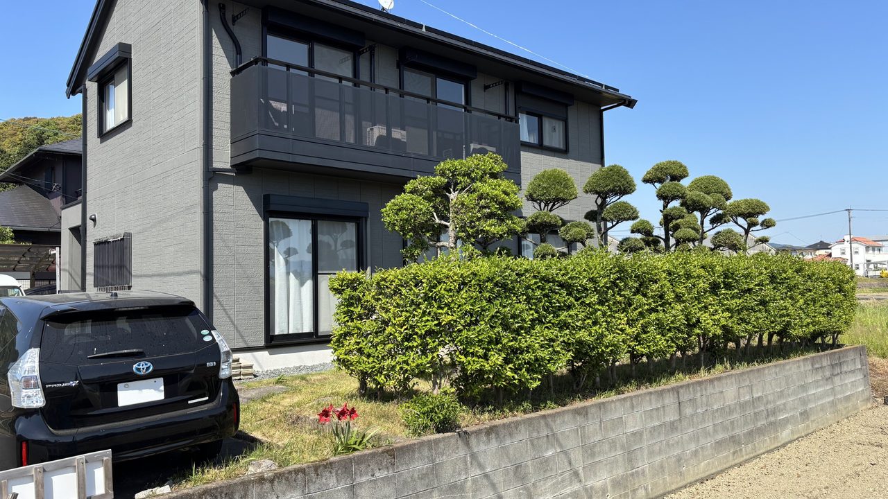福岡県朝倉市の外構リフォーム施工前。敷地の境界に沿ってボリュームのある生垣と庭木が並んでおり、定期的な剪定やお手入れが負担になっていた外観の様子。